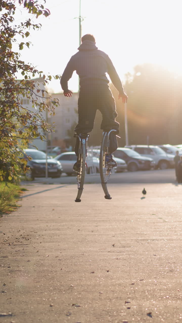 회색 후디와 어두운 회색 바지를 입은 사람이 집으로 둘러싸인 주거 지역에서 해가 지는 동안 다리에 스으로 뛰어내리는 뒤쪽 사진, 도시 에너지, 창의성 및 역동적인 움직임을 보여줍니다.