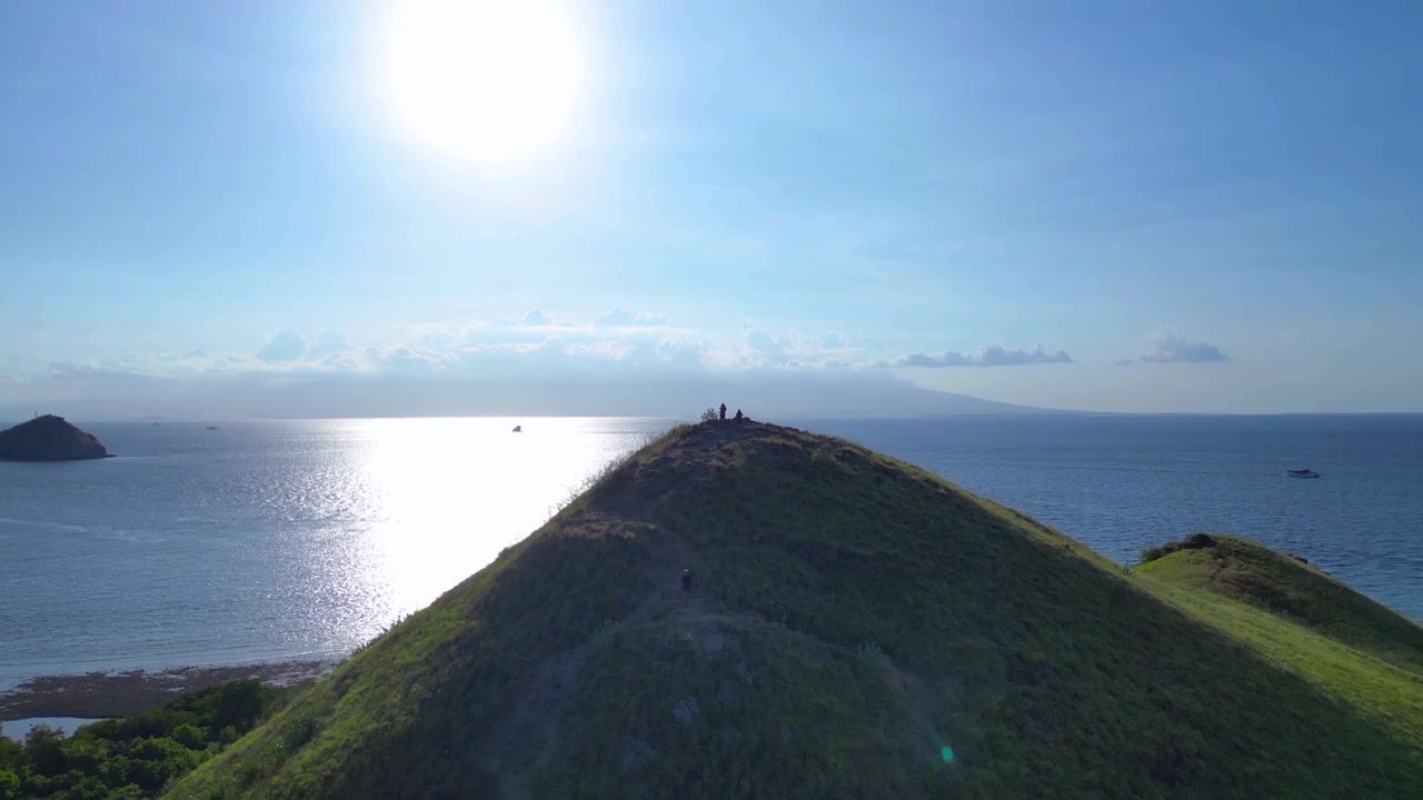 Green island hill overlooking the shallow blue ocean under a bright day sky. Nice aerial view overflight flyover panorama drone