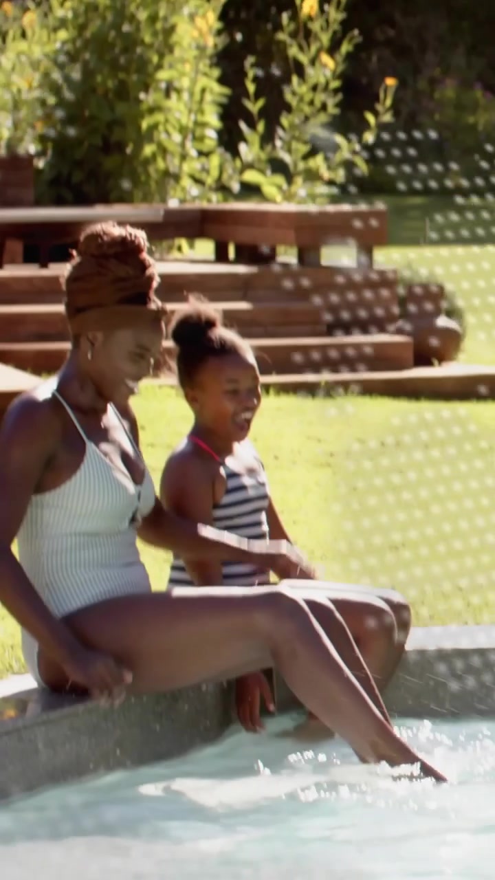 Vertical video: lifestyle mom and girl sitting pool rim dots moving mom dipping toes girl splashing