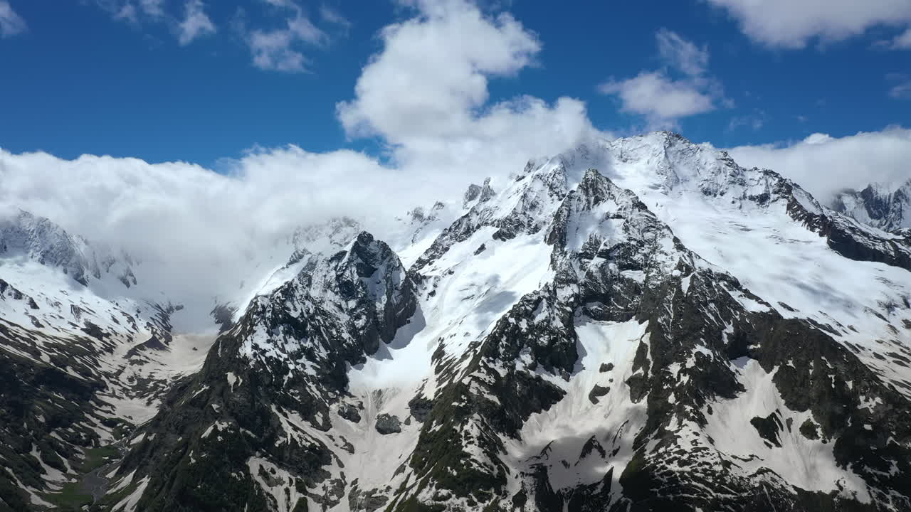 Volo aereo tra le nuvole di montagna sopra splendide vette innevate e ghiacciai.