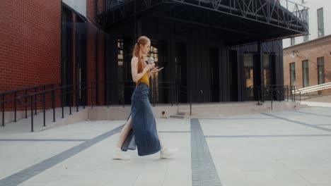 woman walking in urban setting with tablet and drink