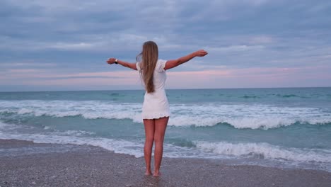 woman in white dress standing on beach with arms outstretched