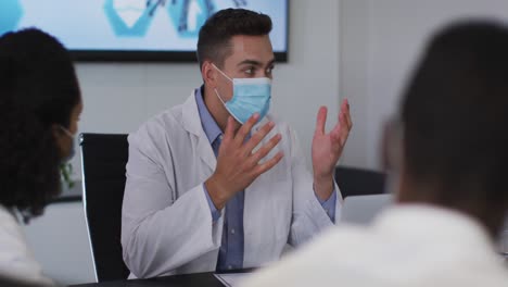 mixed race male doctor wearing mask giving presentation in meeting room gesturing