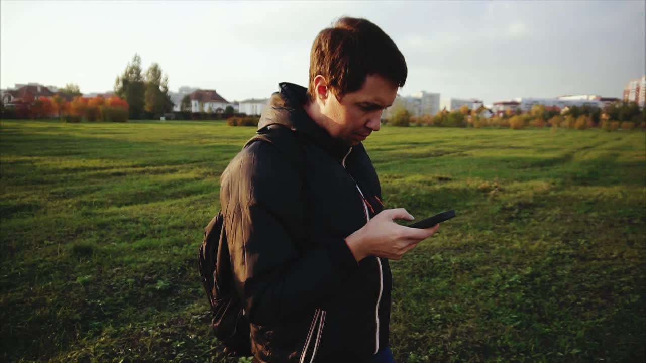 Uomo che usa uno smartphone in un parco al tramonto