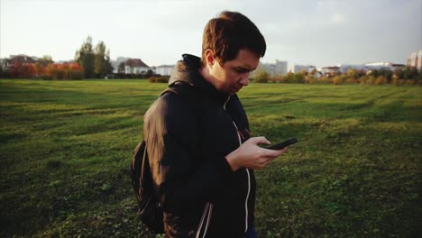 hombre usando un teléfono inteligente en un parque al atardecer