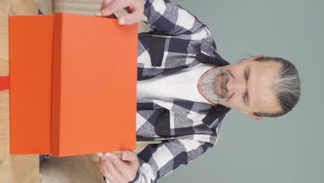 Vertical-video-of-Happy-and-joyful-old-man-opening-gift-package.