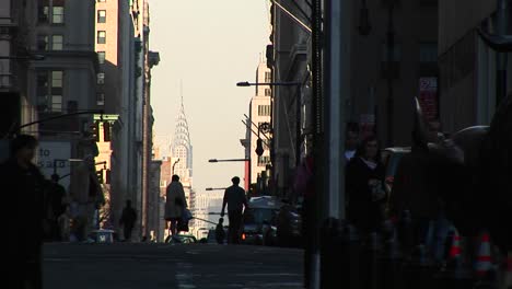 Eine-Belebte-Straßenszene-Mit-Silhouetten-Von-Fußgängern-Im-Vordergrund-Und-Vor-Allem-Wolkenkratzern-Im-Hintergrund