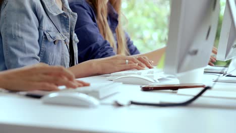una foto de cerca de una mujer de negocios escribiendo a mano y trabajando en la computadora en el escritorio.