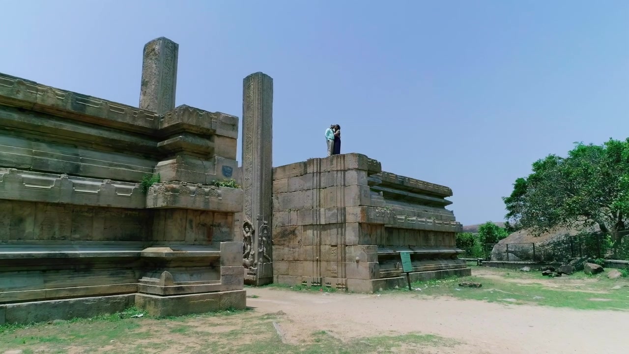 Coppia romantica che si abbraccia sulle rovine del tempio Raya Gopura nel Karnataka, India, con vista aerea in avvicinamento.