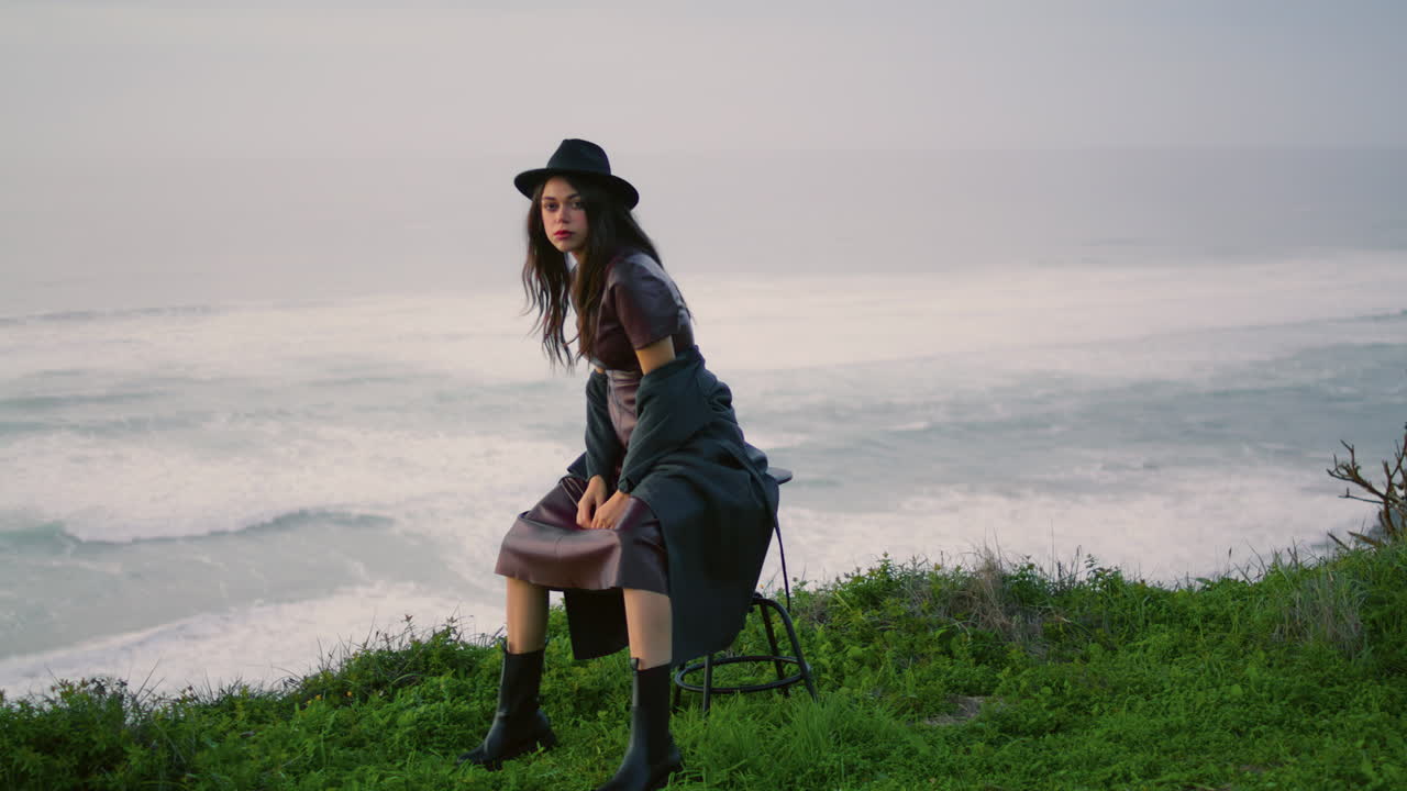 의자에 앉아 있는 실루 스타일리시 모델 해변. 회색 바다에서 포즈를 취하는 여자