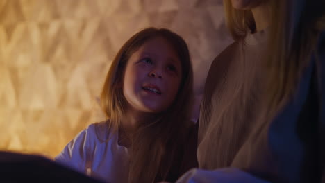 Little-girl-looks-at-mom-reading-book-before-going-to-sleep