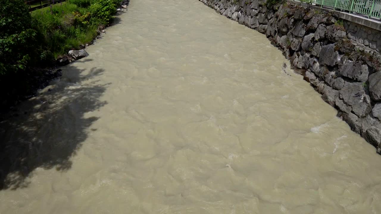 dirty mountain river flowing through the city. Turbulent stream of yellow water