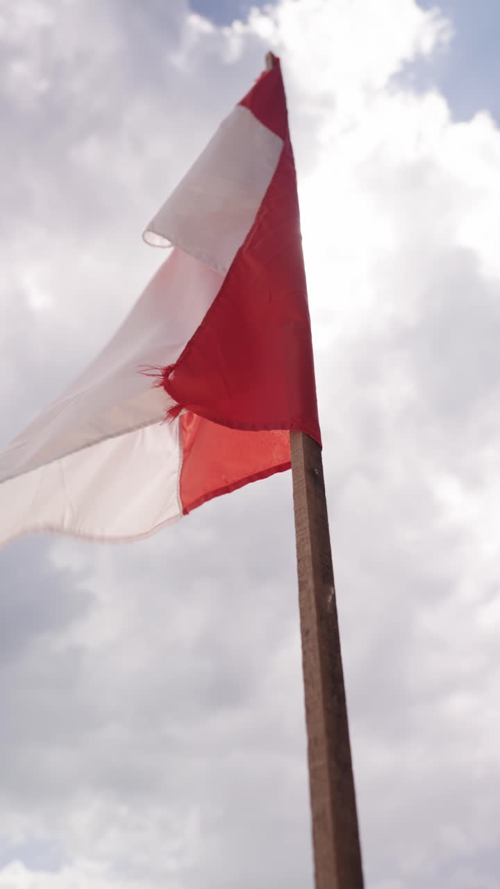 Indonesian flag against sky with sunshine and clouds, vertical view