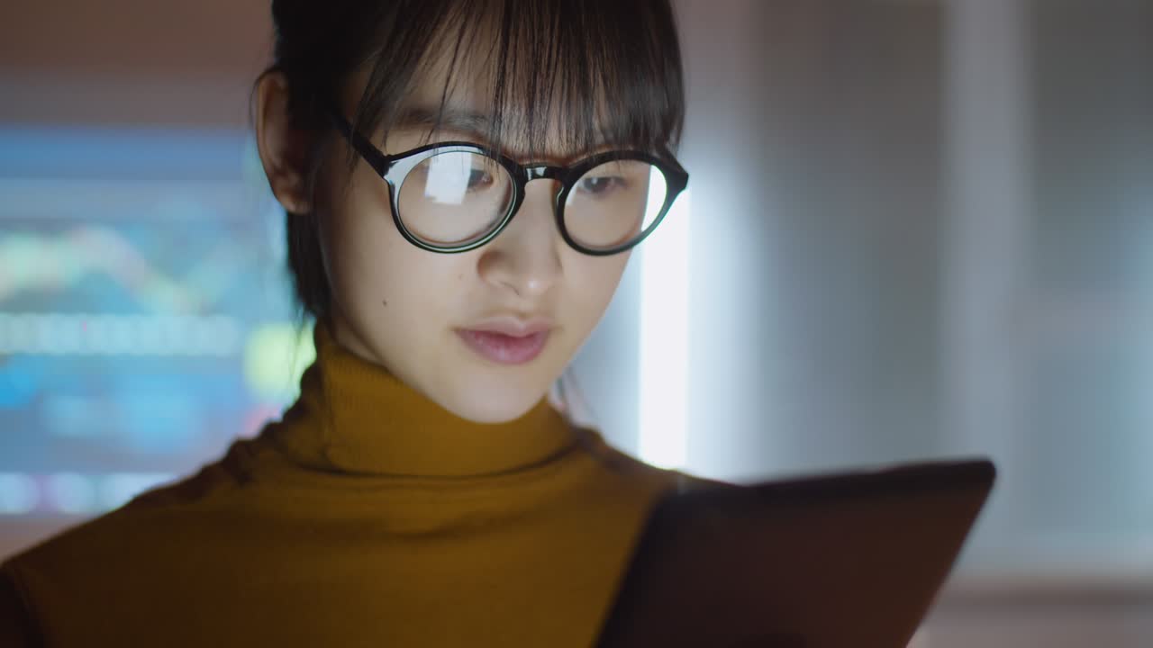 una mujer de negocios asiática usando una tableta digital en una oficina oscura.