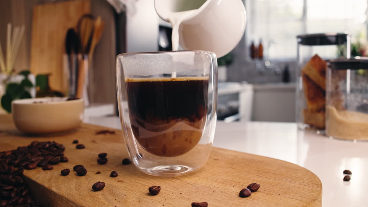 Despejando leite no café em um copo de parede dupla em uma bancada de cozinha