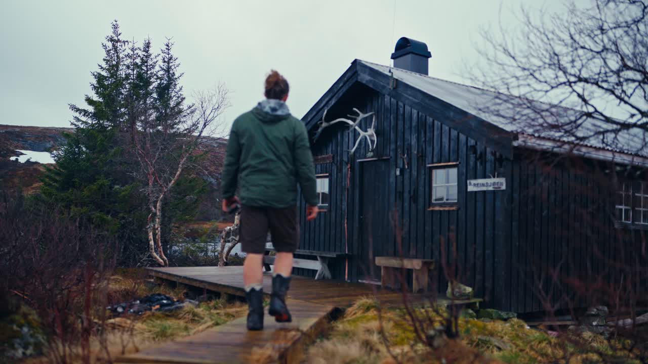Man Walking Towards The Wooden Cabin By The Lake And Mountain In The Early Morning. - static shot