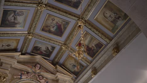 ornate church ceiling with religious paintings and a hanging chandelier