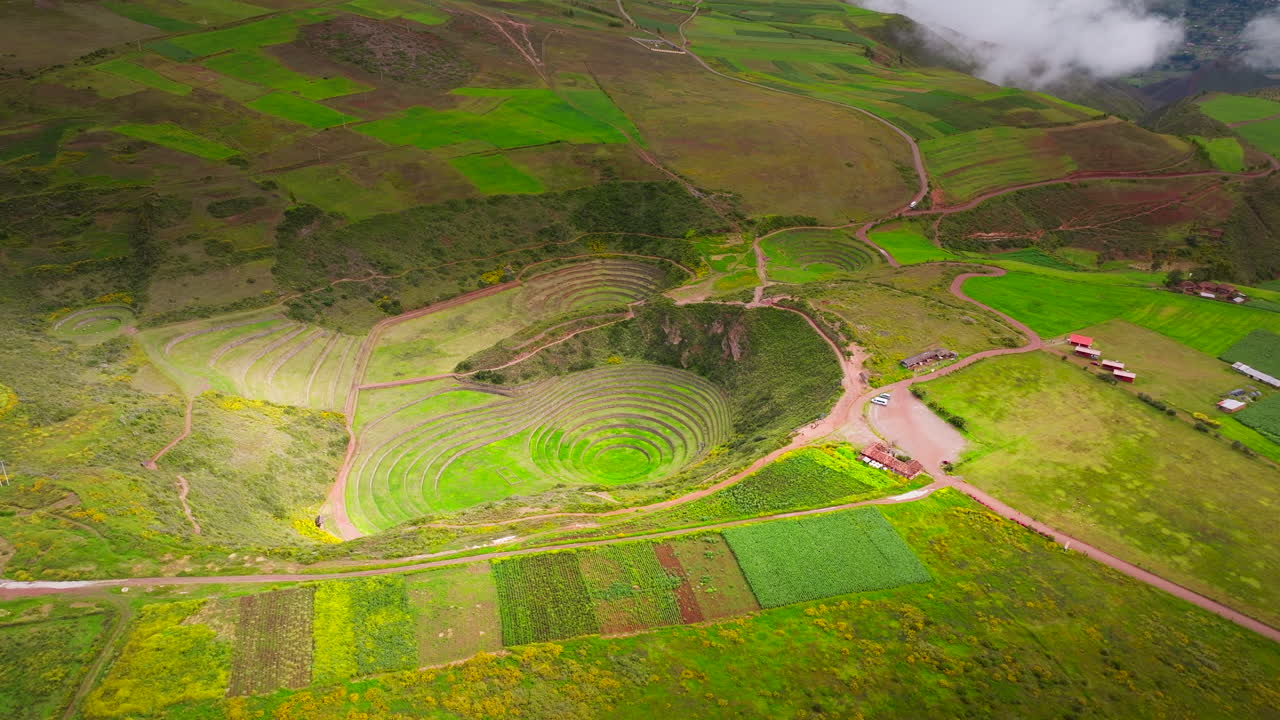 Sito archeologico di Moray nella Valle Sacra vicino a Cusco, Perù, che rivela terrazze Inca concentriche immerse tra vivaci terreni agricoli andini verdi, veduta aerea cinematografica