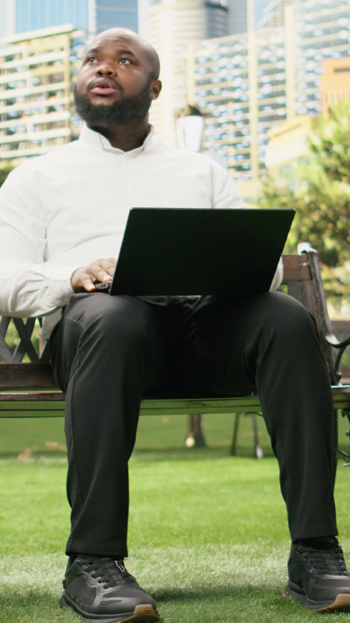 Vertical Video Businessman concentrates on laptop while seated on wooden bench