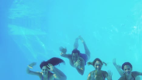 four friends jumping into swimming pool and waving