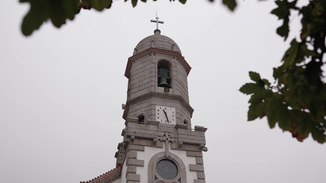 Historic stone church tower with clock and bell under a cloudy sky in Portugal