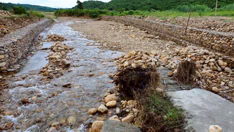 Static-shot-of-rocky-creek-amidst-green-mountains,-flowing-with-water-during-rainy-season