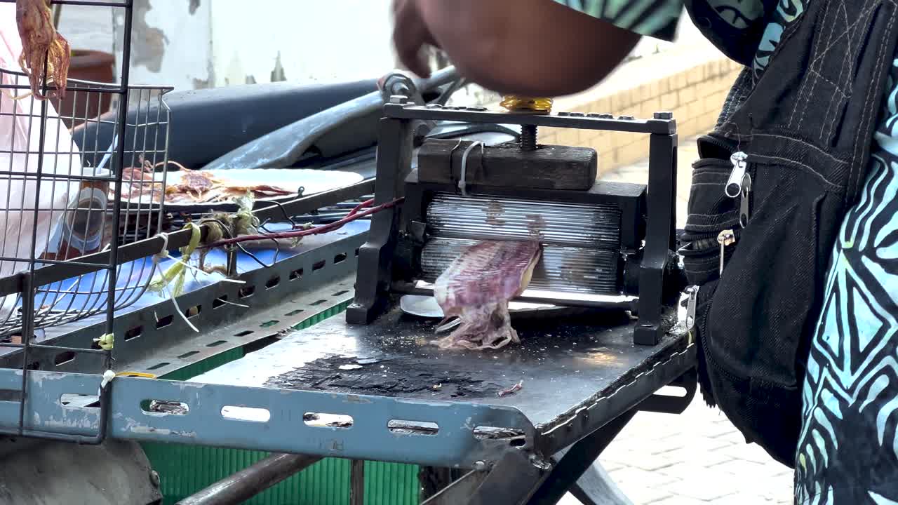 il venditore elabora il calamaro utilizzando una pressa manuale