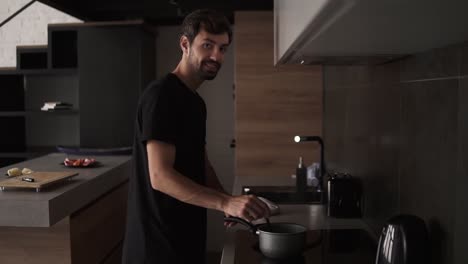hombre positivo cocinando el almuerzo en la cocina de la casa