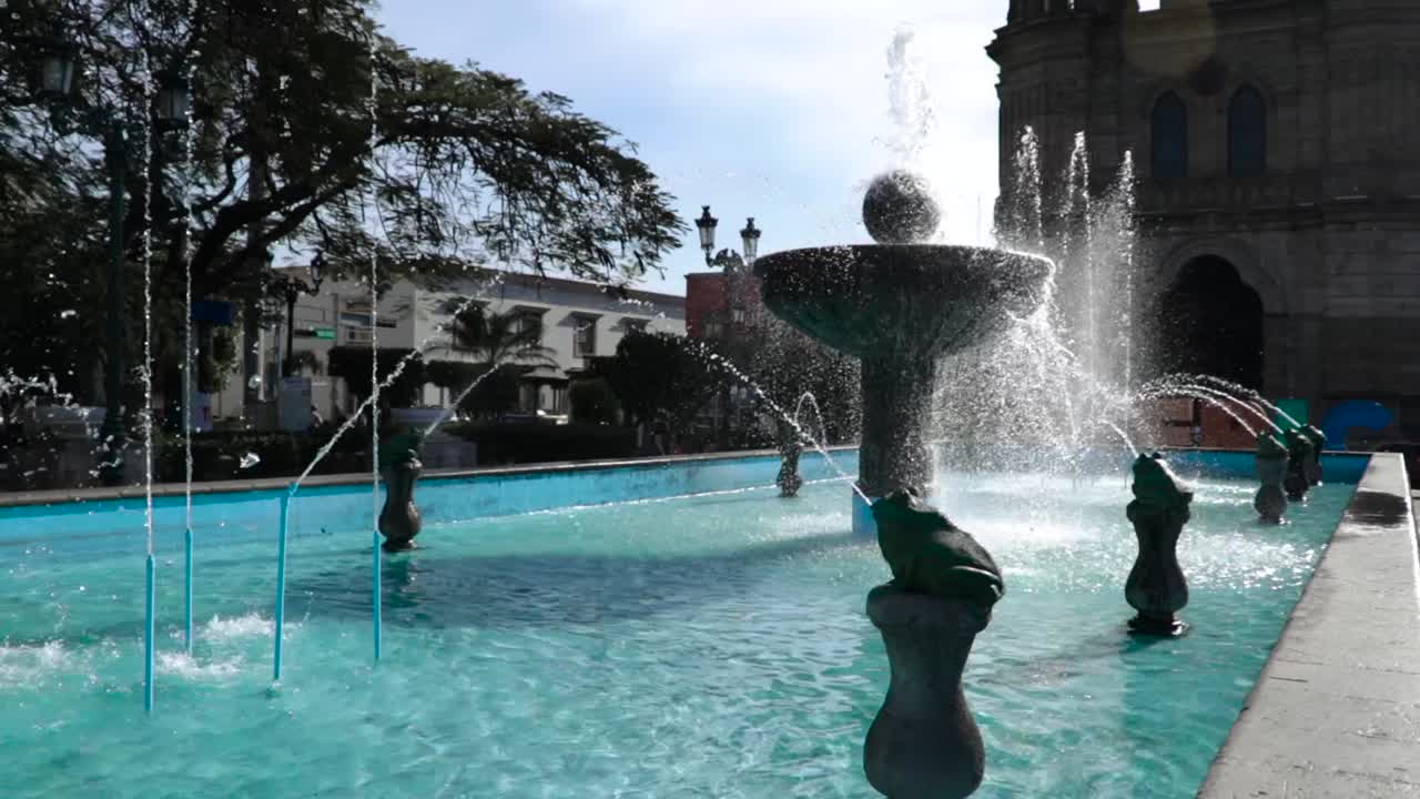 식민지 시대의 멕시코에 있는 작은 마을의 푸른 물이 있는 교회 앞의 큰 분수