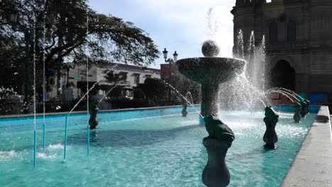 A-big-water-fountain-in-front-of-a-church-with-blue-water-in-a-little-town,-maybe-in-mexico-in-colonial-age