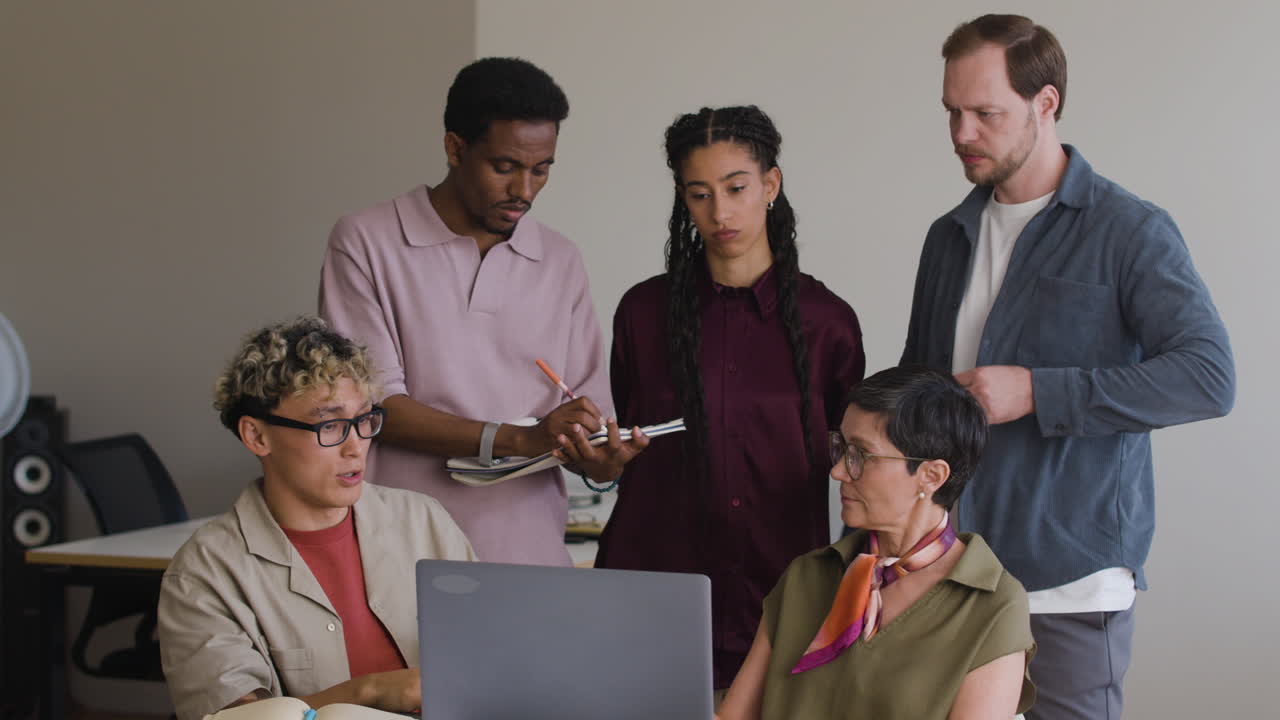 Diverse Business Team Collaborating and Discussing Work Around a Laptop in an Office
