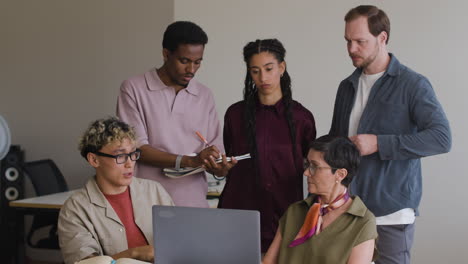 diverse business team collaborating and discussing work around a laptop in an office