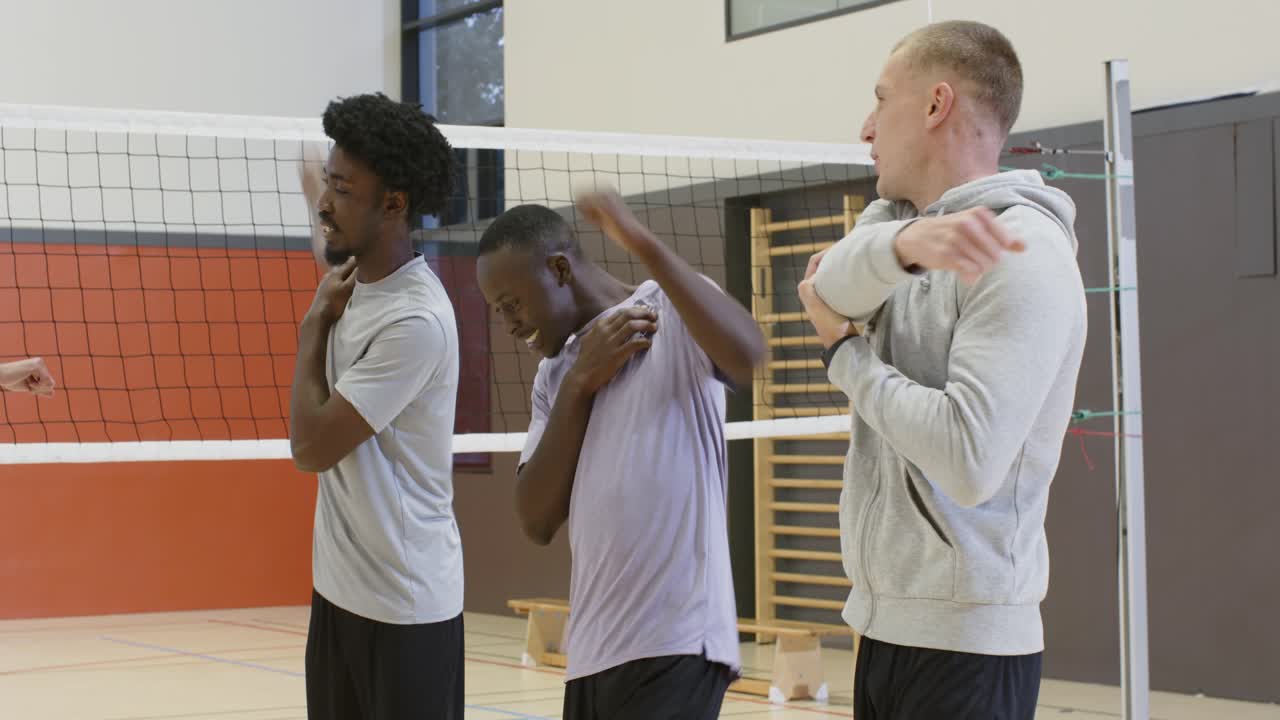 Diverse männliche Spieler führen nach dem Signal des grüngekleideten Spielers Brustklopfen aus und drehen sich am Volleyballnetz, um sich aufzuwärmen.