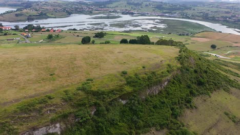 Flug-Auf-Einem-Ebenen-Berg,-Auf-Dem-Sich-Alte-Siedlungen-Befanden,-Mit-Blick-Auf-Einen-Fluss-Und-Berge-Im-Hintergrund-In-Einer-Umgebung-Mit-Grünen-Weiden-Im-Sommer-An-Einem-Bewölkten-Morgen-In-Kantabrien,-Spanien