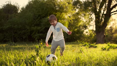 Glücklicher-Junge,-Der-Bei-Sonnenuntergang-Mit-Einem-Fußball-Auf-Einer-Sommerwiese-Läuft.