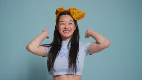 푸른 스튜디오 배경 앞에 있는 젊은 여성이 옷을 입고 사진 부스 스타일의 초상화를 위해 포즈를 취하고 있습니다.