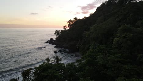 Descending-drone-view-of-a-tropical-beach-at-dusk,-landing-in-the-woods