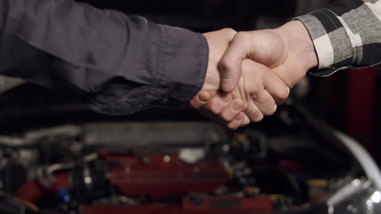 una foto de cerca del mecánico y el cliente estrechando la mano en un taller de reparación de automóviles.