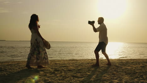 a beach photographer takes pictures of a young woman against the background of the sea and sunset4k