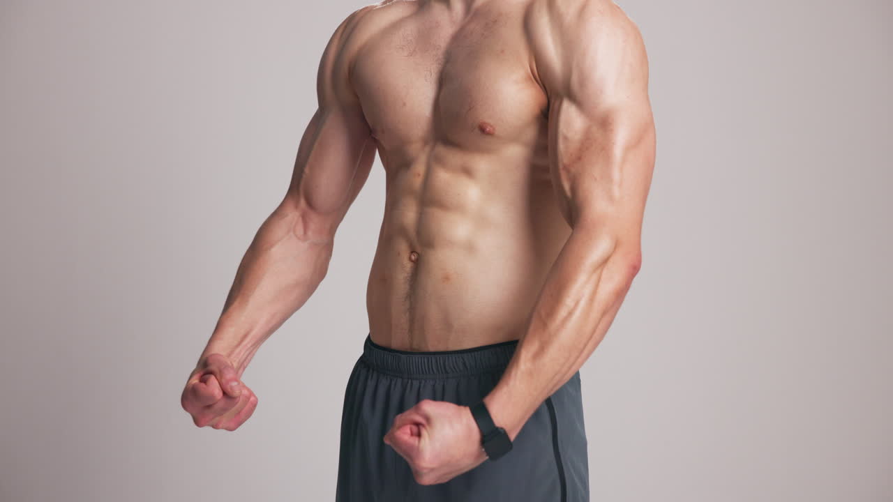 Hombre musculoso mostrando sus bíceps y abdominales en el estudio