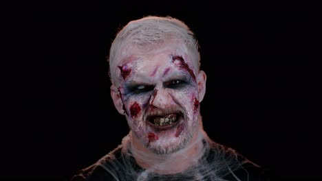 zombie man with wounds scars and contact lenses looking at camera clicks his teeth trying to scare