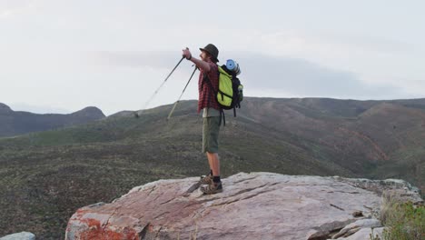 Caucasian-male-survivalist-with-arms-in-the-air-celebrating-reaching-mountain-peak-in-wilderness