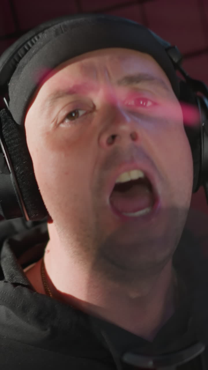 un hombre vestido de negro, cantando apasionadamente en un micrófono en una sala de grabación a prueba de sonido. su rostro muestra una expresión intensa mientras hace un gesto de la mano, completamente inmerso en la actuación