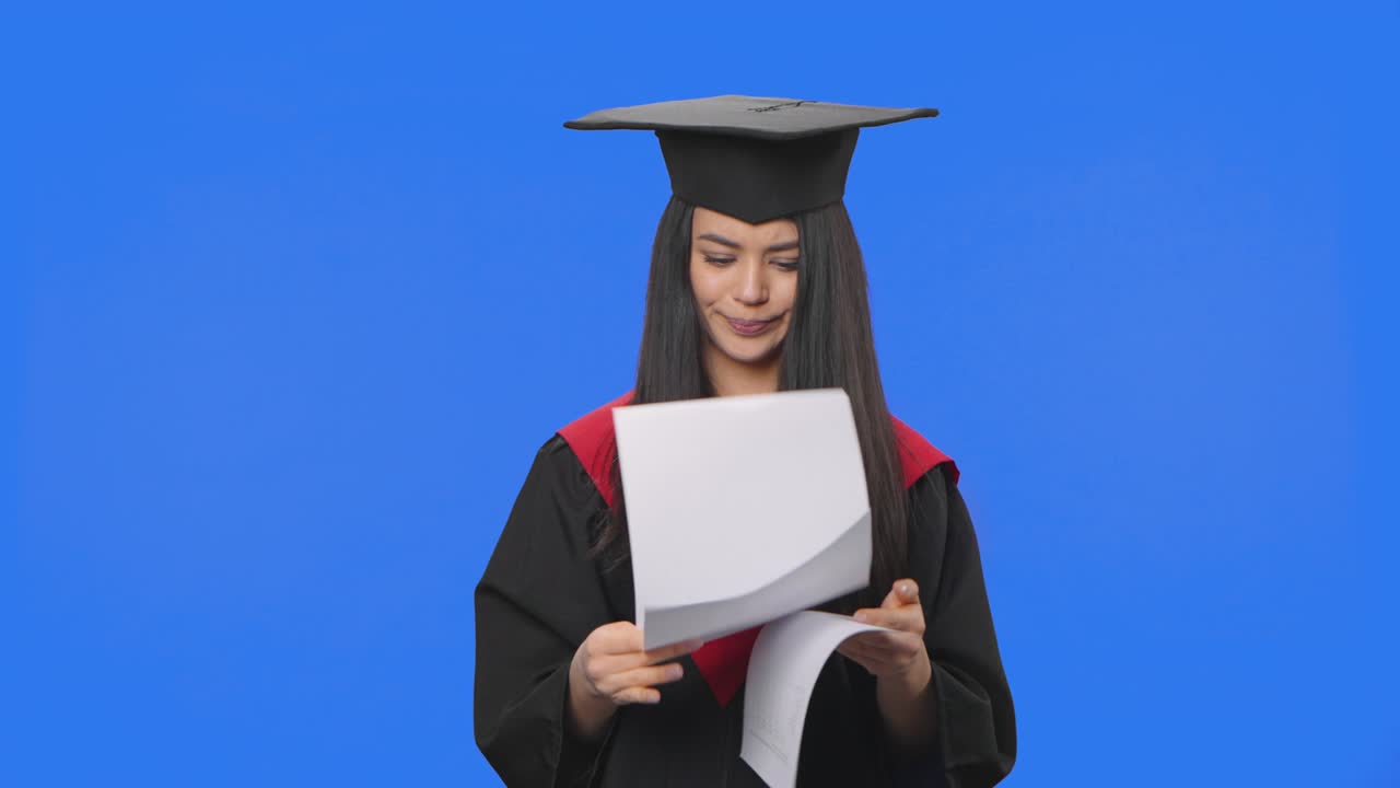 retrato de una estudiante en traje de graduación, mirando a través de documentos, rasgándolos y tirándolos. joven posando en el fondo de la pantalla azul. de cerca. cámara lenta lista 59.94fps