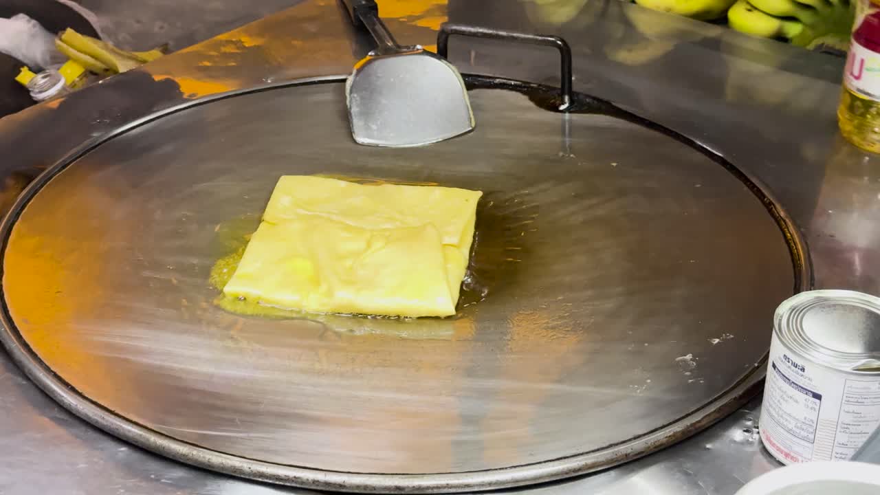 A street vendor prepares Thai roti on a hot griddle in Phuket, Thailand, showcasing traditional street food techniques and vibrant local culture