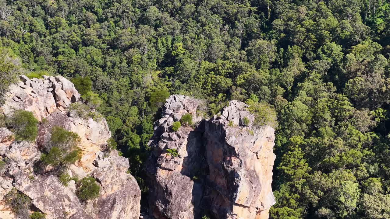Aerial footage showcasing the rugged Nimbin Rocks surrounded by lush greenery under bright sunlight in Nimbin, NSW, Australia