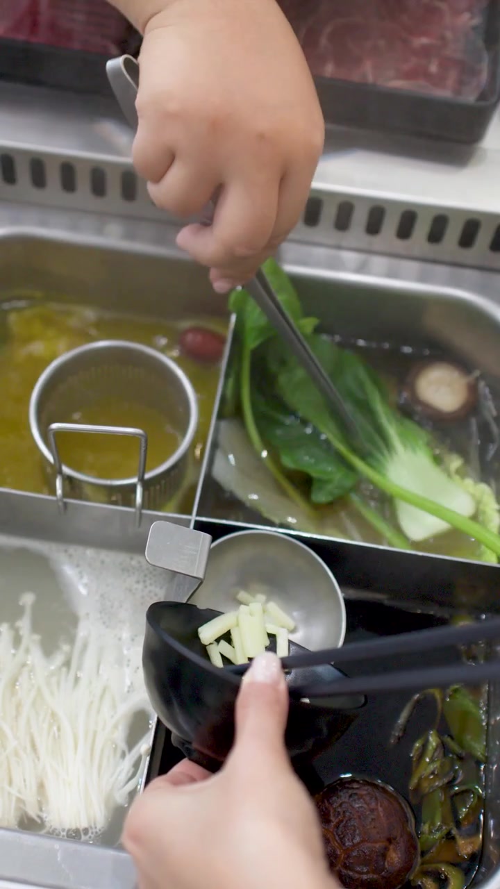 出汁、葉物野菜、キノコが入った仕切りのある鍋に、人が刻んだニンニクを加えている。