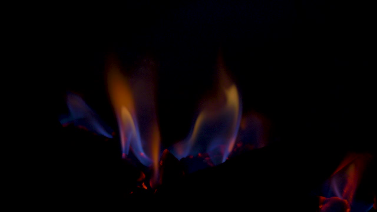Slow motion close-up shot of gas fireplace hot flames burning embers on charcoal coal fake wooden logs behind glass panel household heating energy