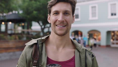 retrato de un joven guapo que busca sonriendo alegremente en la cámara sosteniendo una bebida de café de fondo urbano