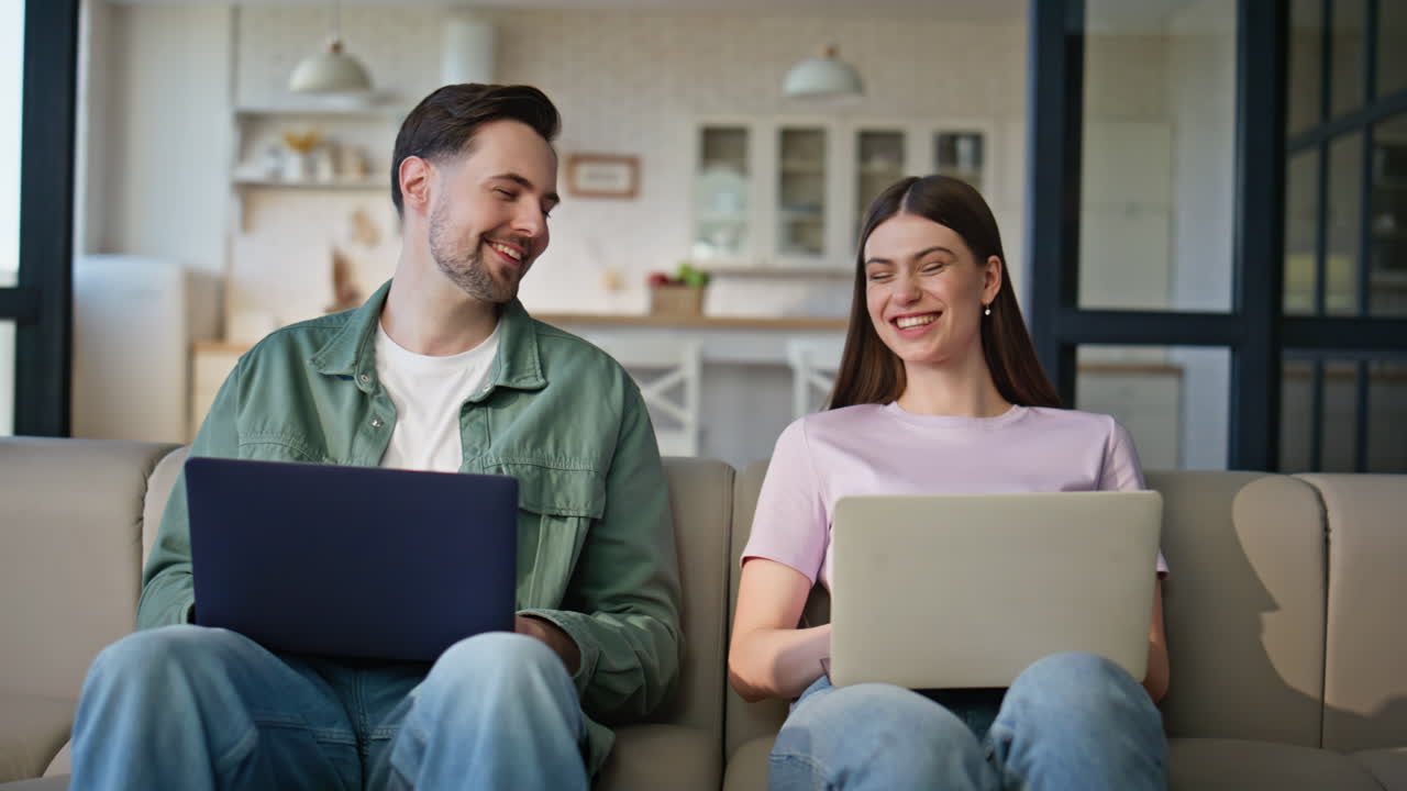 Home sweethearts browsing laptops at soft couch place. Young couple working
